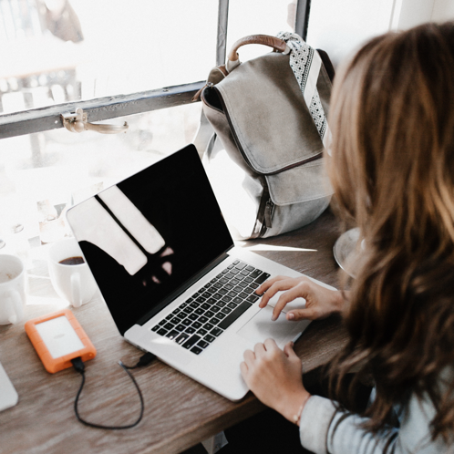 Fotografía En Primer Plano De Una Mujer Sentada Junto A La Mesa Mientras Usa Macbook